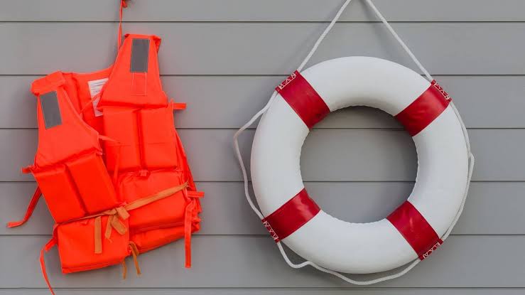 Gilets de sauvetage orange et bouée blanche accrochés à un mur gris